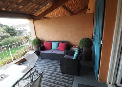 cette image représente une grande terrasse colorée équipée salon canapé, table et chaises, plantes vue jardin